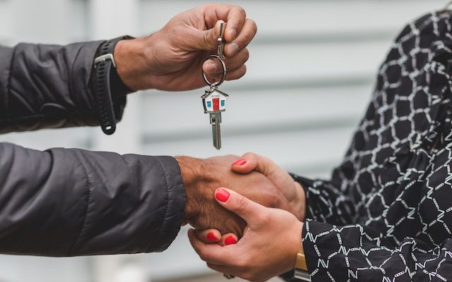 Two persons holding each other's hands and the key to a new house